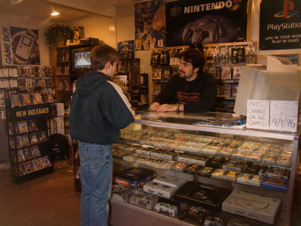 A teen talking with the clerk across a glass game-shop counter full of cartridges