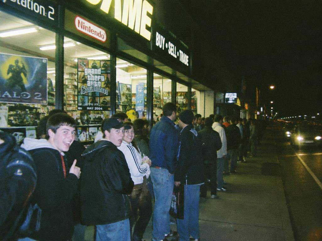 A line of fans outside a lit game store at night for a midnight launch