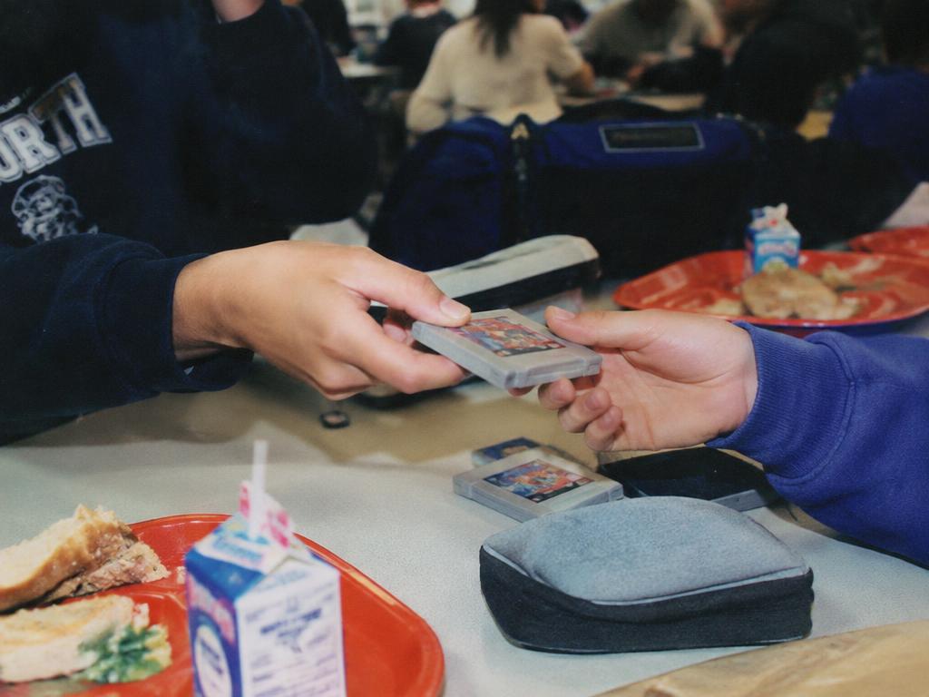 Hands trading a game cartridge across a school cafeteria table
